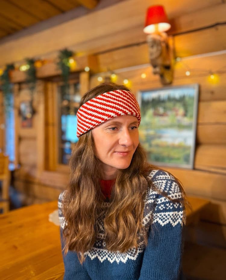 Ira in a hand-knit Nordic sweater and a red and white striped headband, in a wooden cabin